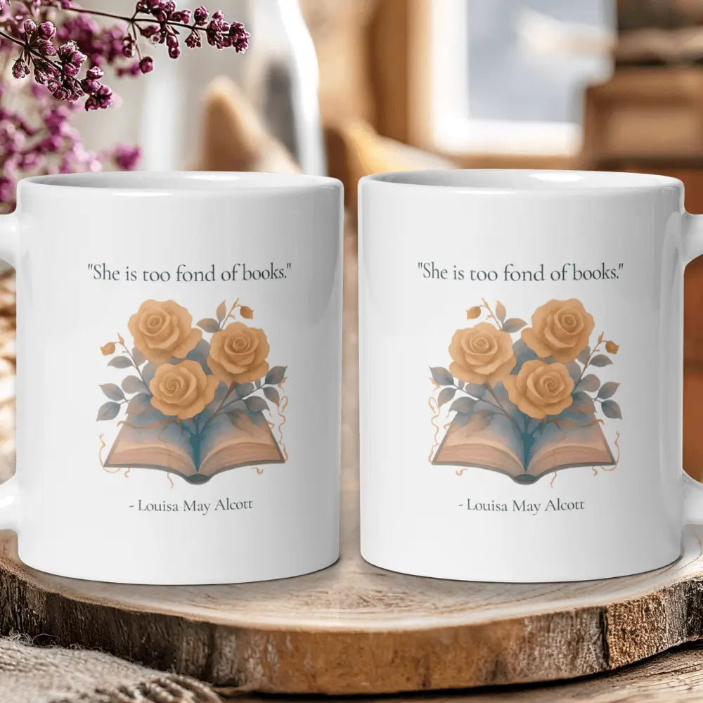Two white ceramic mugs displayed side by side on a rustic wooden slice. Each mug features a printed design of an open book with yellow roses and the quote, 'She is too fond of books.