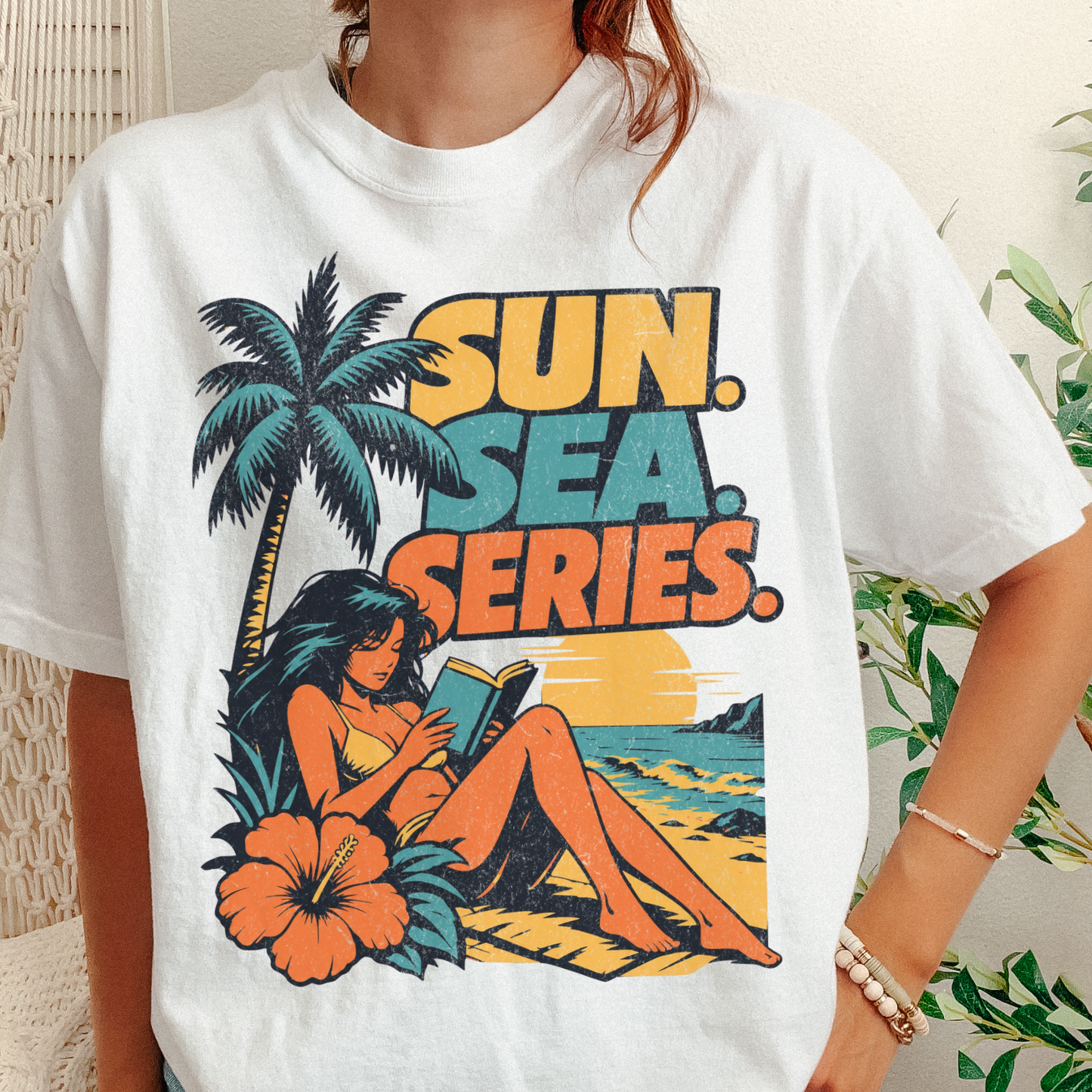 A person wearing a white graphic T-shirt with a retro beach scene and the text 'SUN. SEA.
