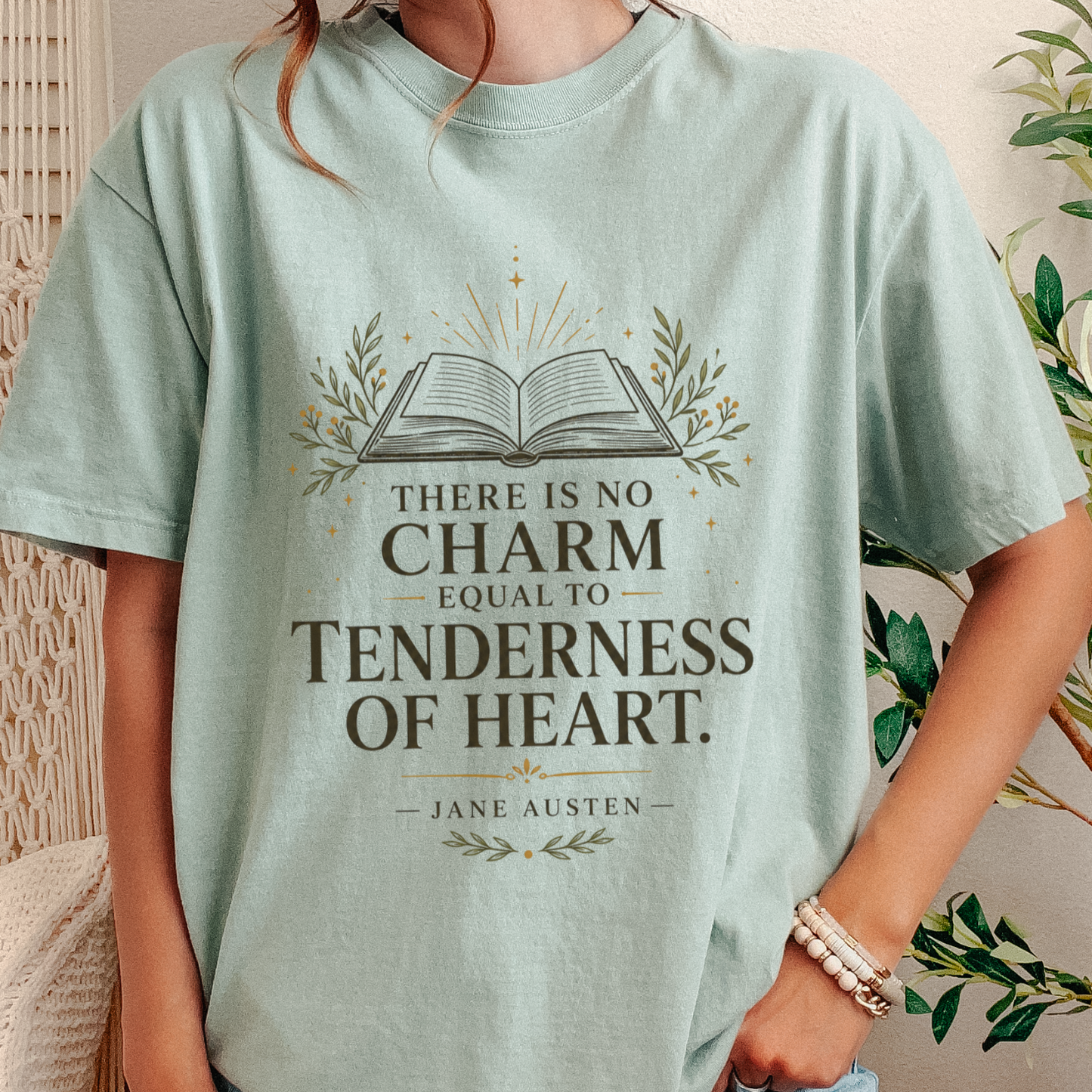 A person wearing a light mint green graphic T-shirt with a book illustration and the quote 'There is no charm equal to tenderness of heart. Jane Austen.